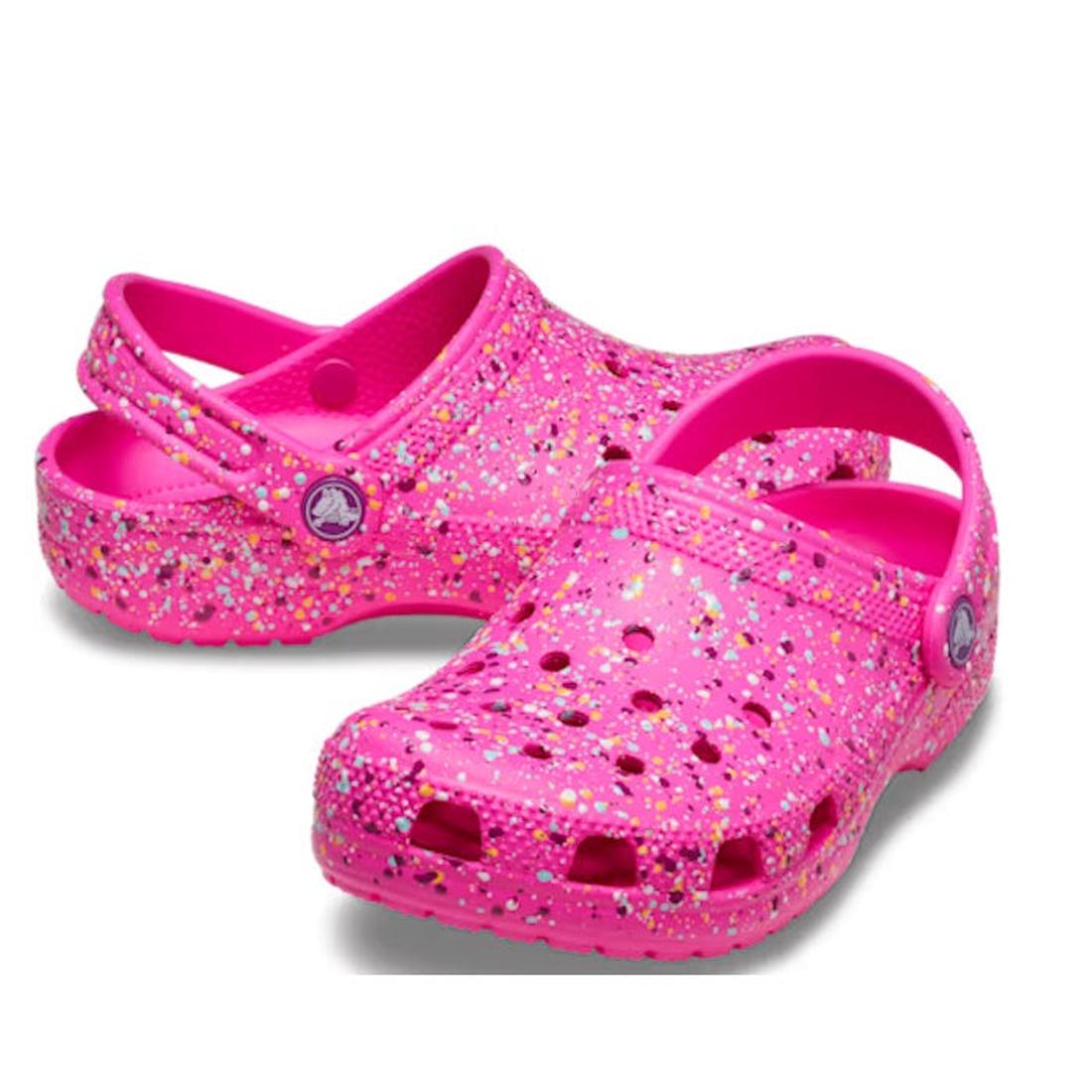 The Crocs Kids - Youths Classic Clog K Paint Splatter Print Bright Pink Multi features ventilation holes and an adjustable heel strap, adding playful style to any outfit with its vibrant paint splatter design.