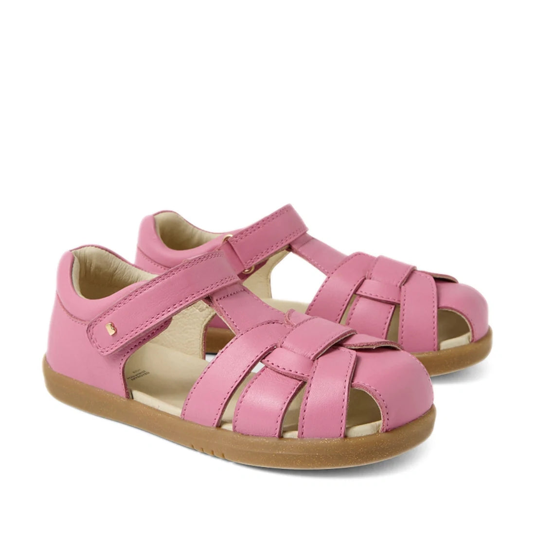 The Bobux Kids Plus KP Skip Twist Cashmere Rose Pink Closed Toe Sandal is a pair of pink leather children’s sandals featuring closed toes, tan rubber soles, and adjustable Velcro straps over the top and around the ankles—perfect kids’ summer shoes that pr