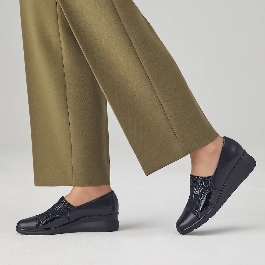 A person stands on a light gray floor wearing olive green pants and Pitillos Womens Lycra and Patent Leather Shoe 10731, featuring a black wedge heel, subtle textured pattern, and removable innersole, against a plain background., 8445191655554, 8445191655