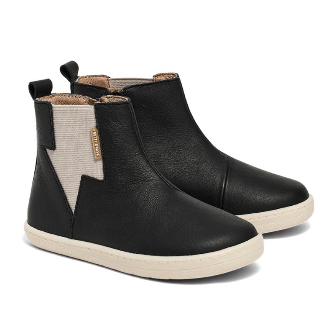 A pair of Pretty Brave Electric Leather Boot - Jet Black, ankle-high with white elastic side panels, cream rubber soles, and a subtle lightning bolt design, displayed on a white background.