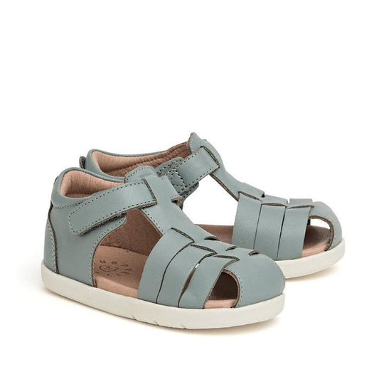 The Pretty Braver Billie First Walker Sandal in Seafoam features a light blue shade, white soles, Velcro straps, and front and side cut-outs—ideal for early walkers. Closed-back design shown angled on a plain white background.