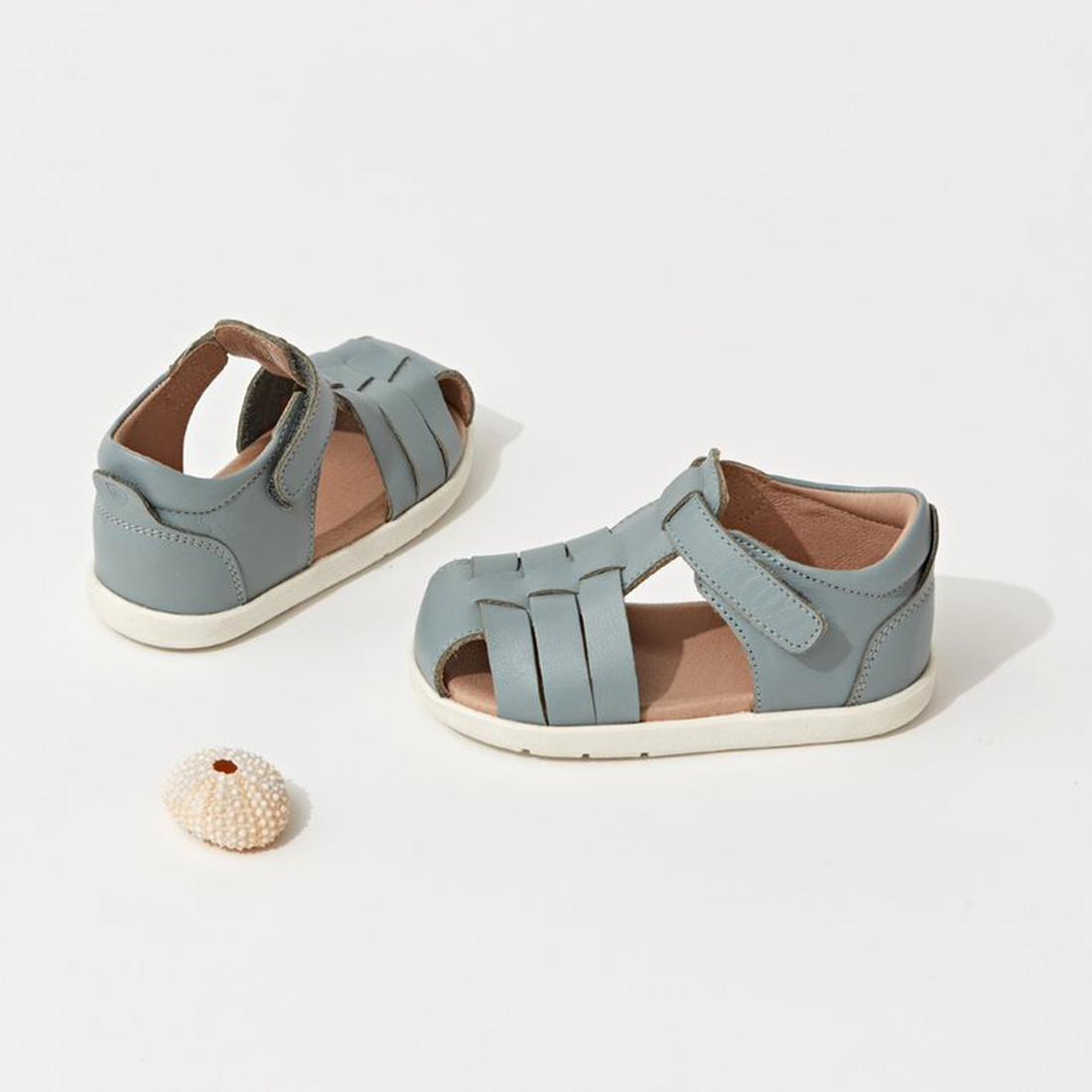A pair of Pretty Braver Billie First Walker Sandal Closed Back in Seafoam, ideal for early walkers, are displayed on a white surface beside a small sea urchin shell., 9421036357202, 9421036357219, 9421036357196