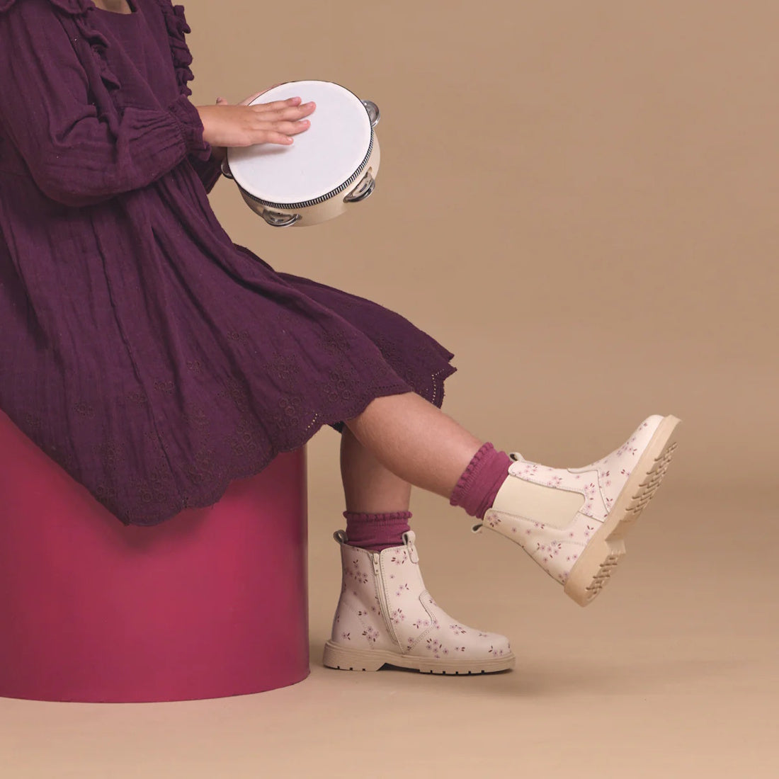A child in a purple dress and Pretty Brave Girls Hudson Winter Bloom Pink Leather Boots sits on a magenta stool, holding a tambourine against a beige background., 9420075363205, 9420075363199, 9420075363182, 9420075363175, 9420075363168, 9420075363151, 94