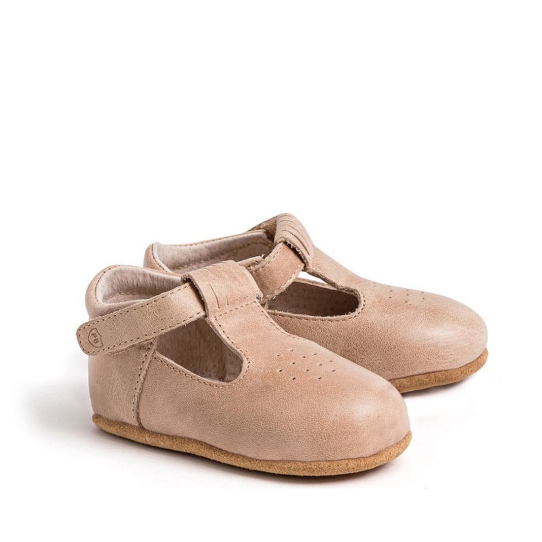 A pair of Pretty Brave Morgan T Bar Taupe baby shoes, made from natural leather in light brown, featuring classic T-bar straps with Velcro closures, soft soles, and small perforated details on the top.