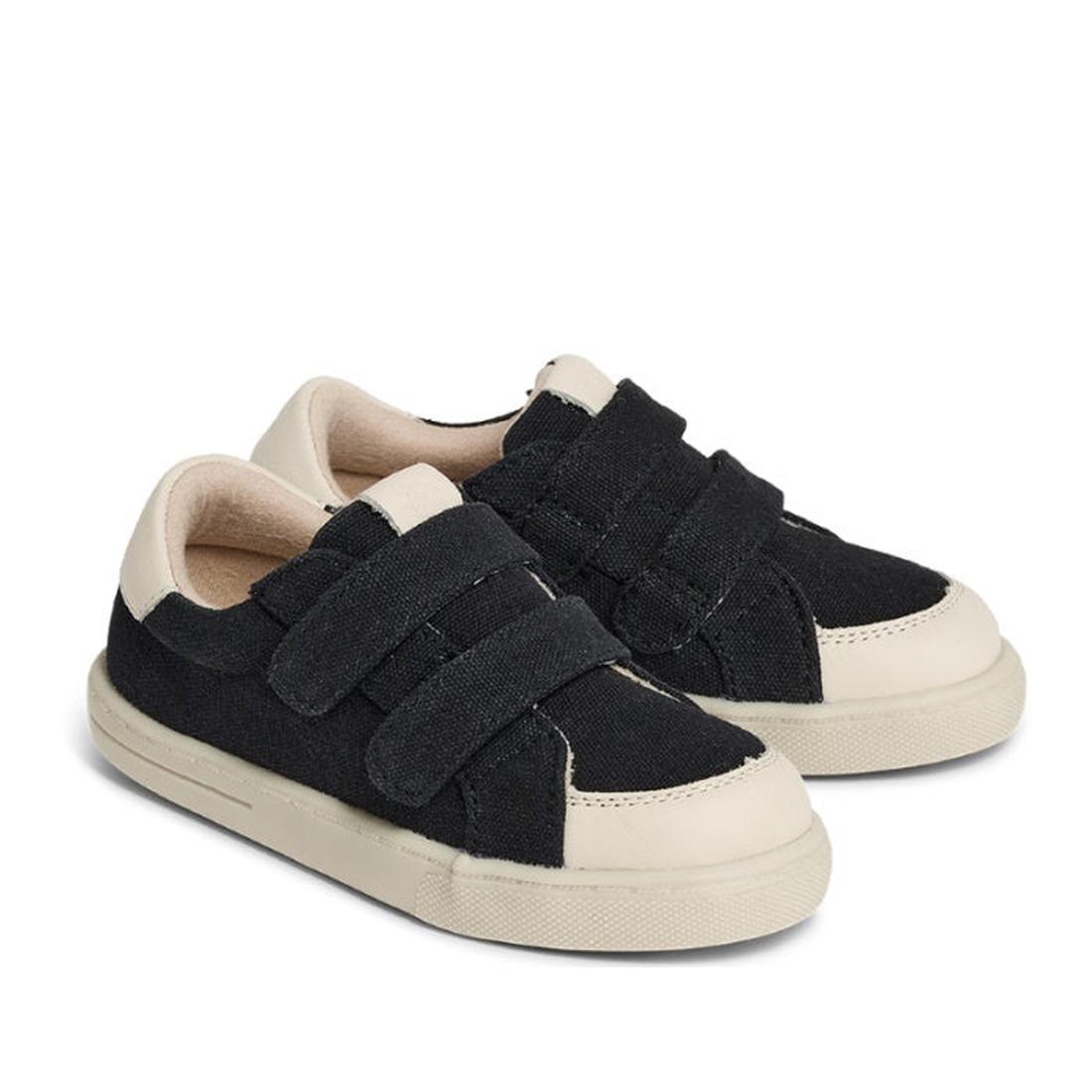 A pair of Pretty Brave Otto Organic Canvas Trainers in black with leather toe buffer, white soles, bamboo cotton lining, and two velcro straps per shoe, displayed on a white background.