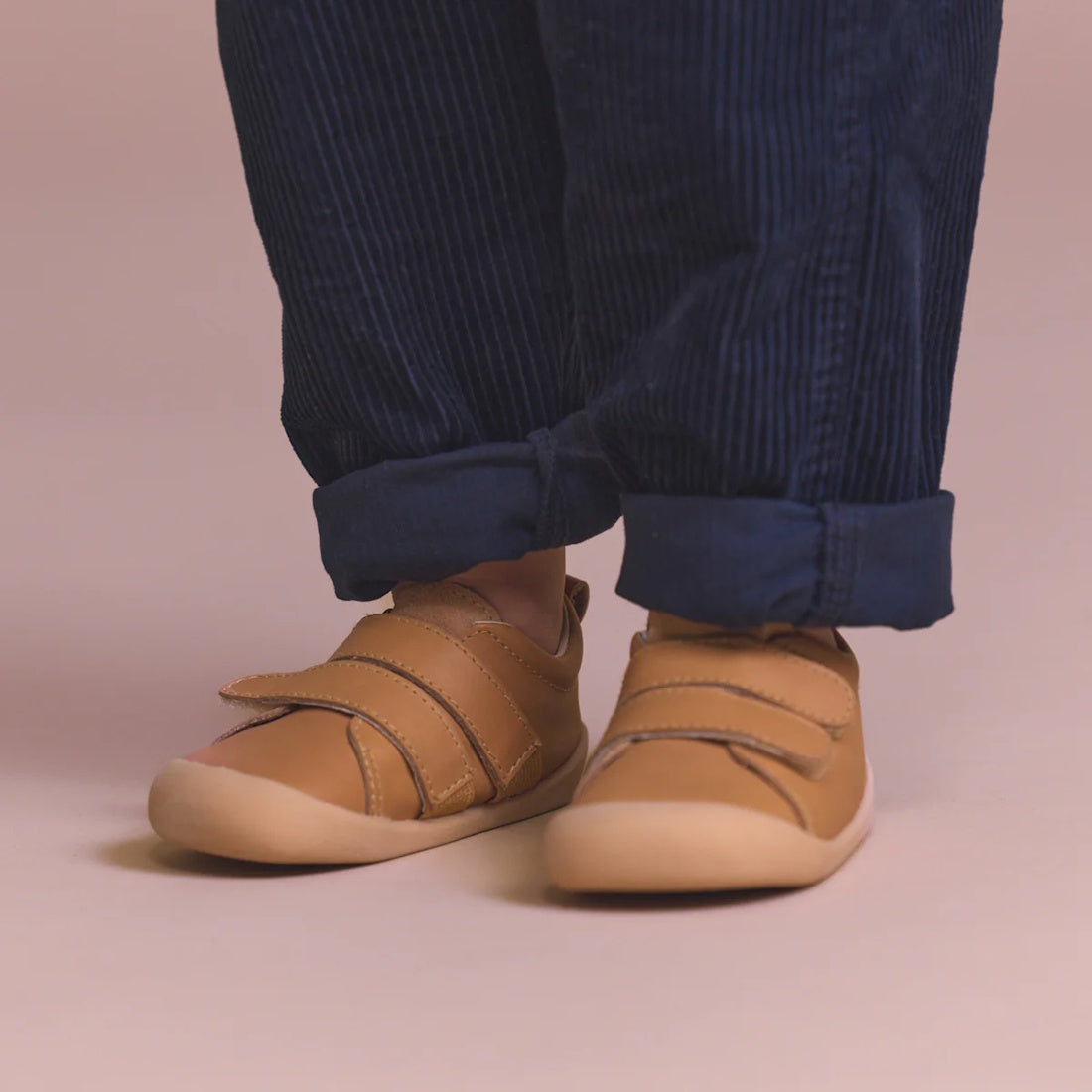 A child wearing cuffed blue corduroy pants and Pretty Brave First Walker Toto Leather Trainer Tan shoes stands on a light pink surface., 9420075366183, 9420075366176, 9420075366169, 9420075366152, 51694