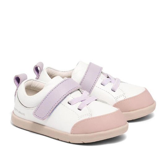 The Pretty Brave Boston Leather Trainer First Walker White Blush features white uppers, light pink soles and toe caps, and lavender laces and straps—ideal stylish sneakers for toddlers learning to walk, shown on a plain white background.