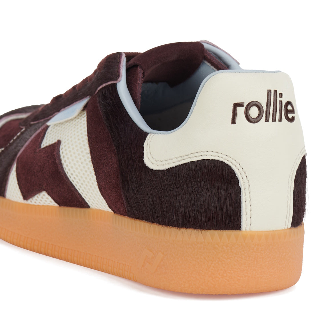 A close-up of the Rollie Womens Pace Dark Cherry Bone Suede Sneaker features a brown and white furry upper, light brown rubber sole, and "rollie" embroidered on the white heel tab., 9339554000315, 9339554000317, 9339554000164, 9339554000056, 9339554000182