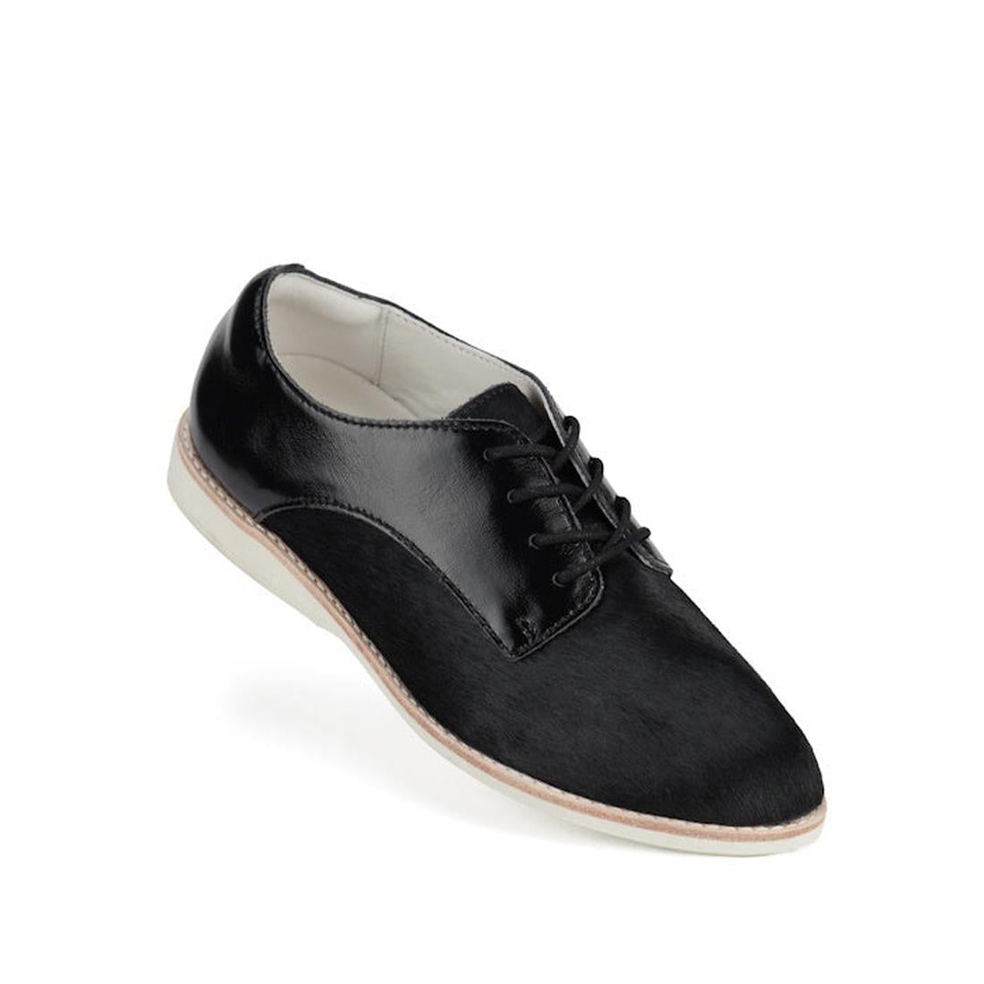 The Rollie Womens Derby Black Splice Leather Brogue Shoe features black leather, black laces, a white interior, a light-colored sole with an anti-slip rubber outsole, and is displayed against a white background.