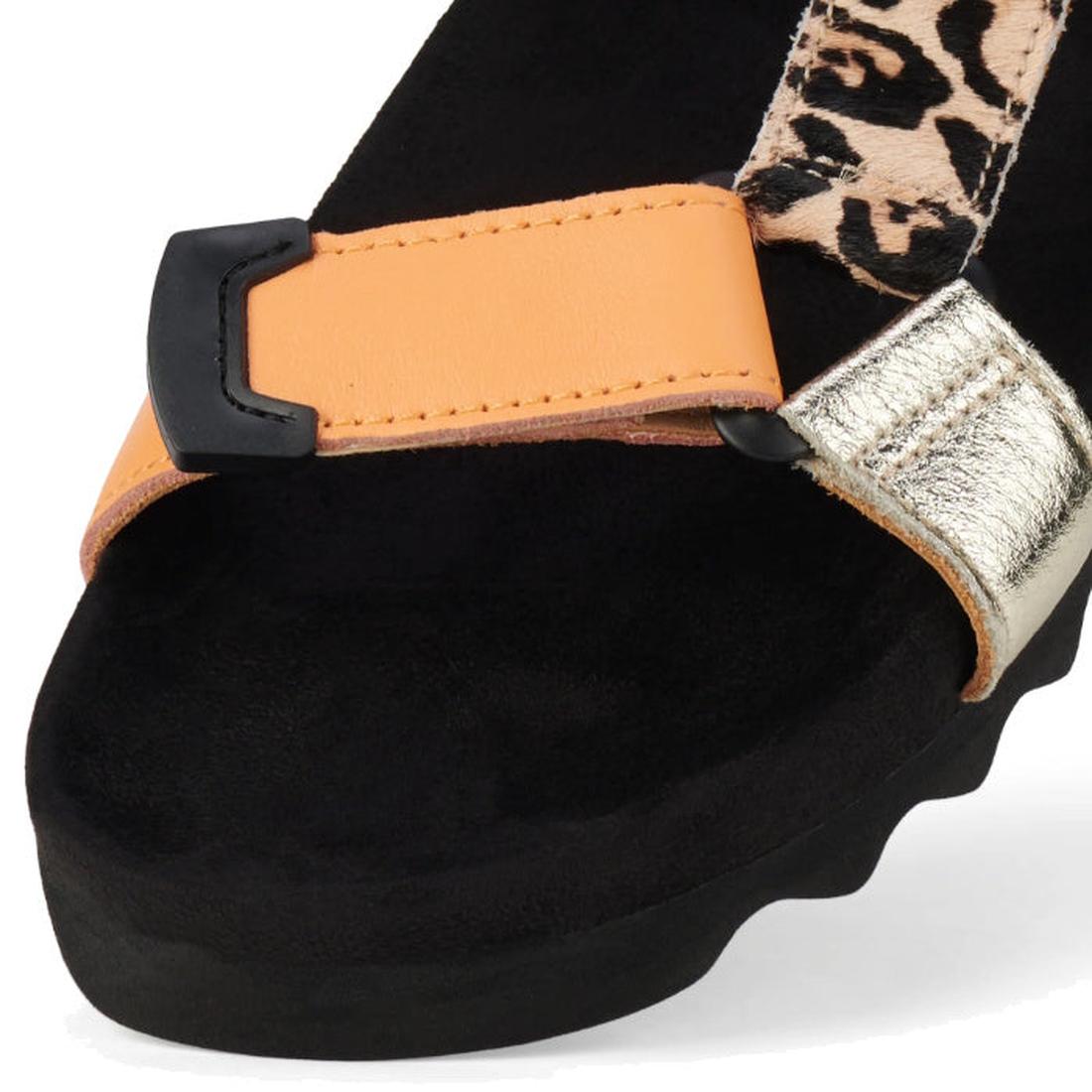 A close-up of the Rollie Womens Sandal Tooth Wedge Leopard Multi, featuring adjustable orange, metallic gold, and leopard print leather straps on a black suede footbed with a wavy sole edge., 9339554333786, 9339554333793, 9339554333809, 9339554333816, 933