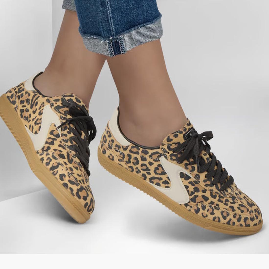 A person in rolled-up blue jeans and Skechers Womens HotShot On The Prowl Leopard Suede Sneakers with beige soles, black laces, and Air-Cooled Memory Foam stands against a plain light background., 52252, 199025014359, 199025014373, 199025014380, 199025014