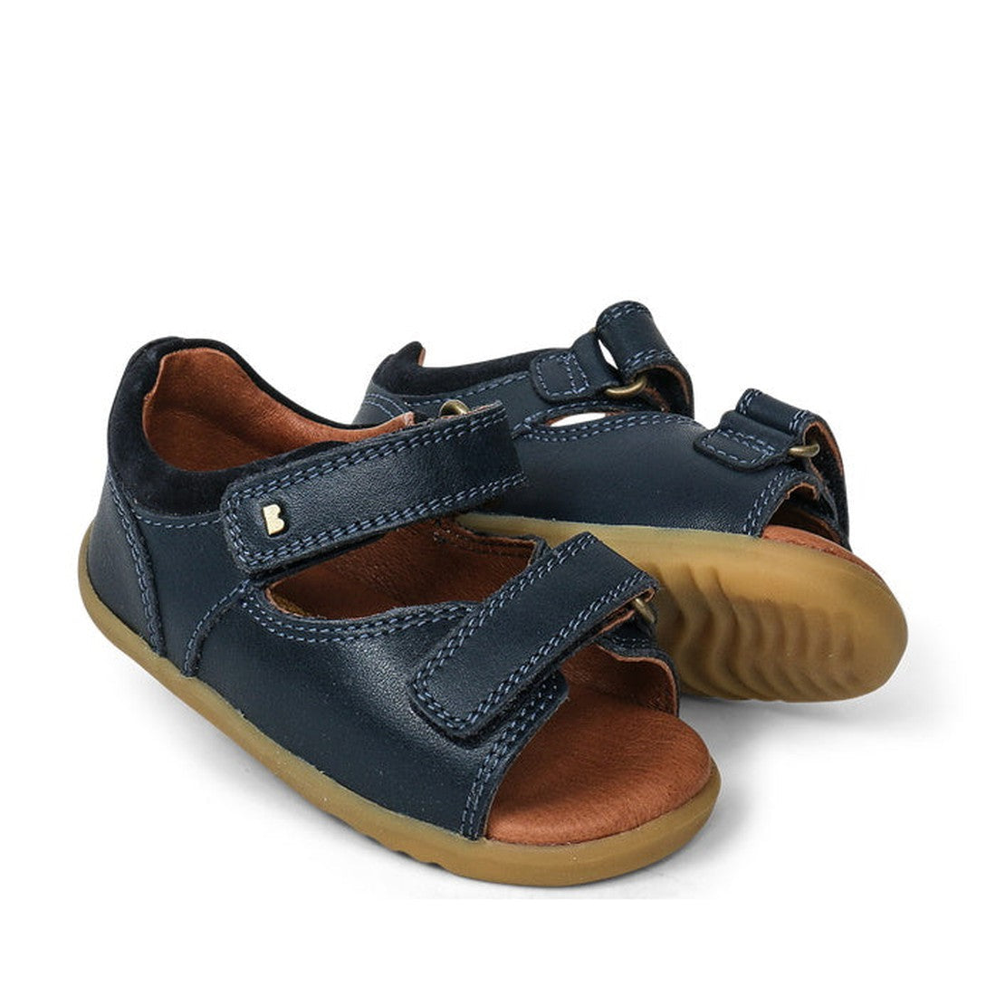 The Bobux Step Up - Driftwood 728607A Navy are navy leather first walker sandals with velcro straps, tan rubber soles, open toes, and a small metallic heart detail—ideal for little feet on the move.