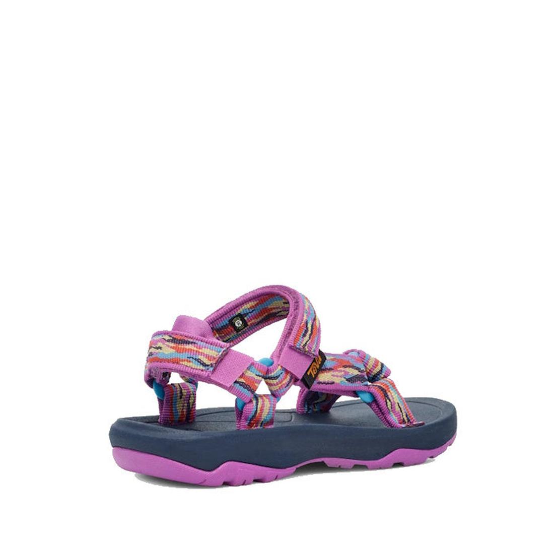 The Teva Kids K Hurricane XLT2 Girls Active Sandal in Purple features colorful purple, pink, and blue patterned straps, an open toe, a dark blue footbed, and a purple sole. Shown from a rear side angle on a white background. Vegan-friendly design., 196565