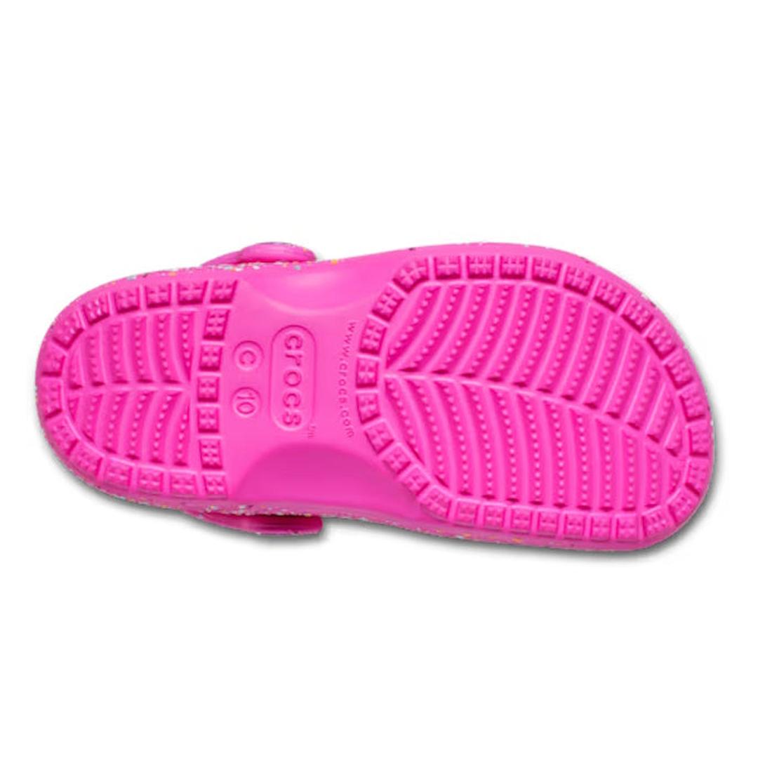 The image shows the bottom view of the Crocs Kids – Toddlers Classic Clog K Paint Splatter Print in Bright Pink Multi, featuring a textured sole for grip and the Crocs logo embossed at the center. These lightweight shoes provide comfort and fun style., 19