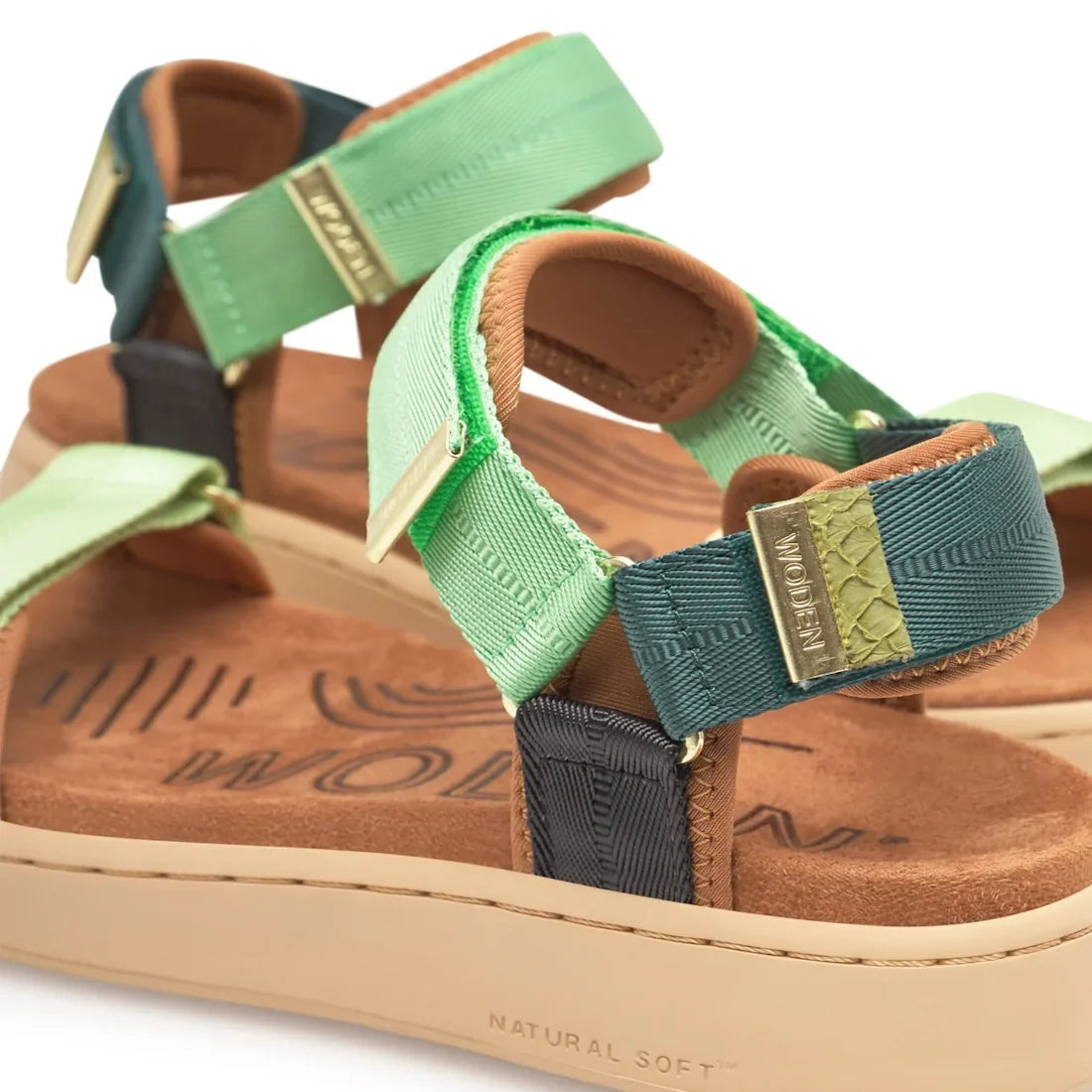 A close-up of the Woden Line Women's 3 Strap Sandal in Apple Green, featuring platform soles, green and teal fabric straps, adjustable Velcro closures, and tan cushioned footbeds with a printed design. Part of our eco-conscious footwear collection, these 
