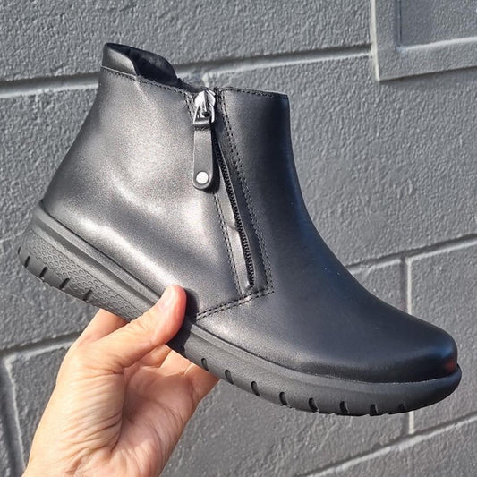 A caring hand displays the Ziera Solange XF black leather ankle boot for women, with easy side zipper and comfy rubber sole outdoors.  ksnz